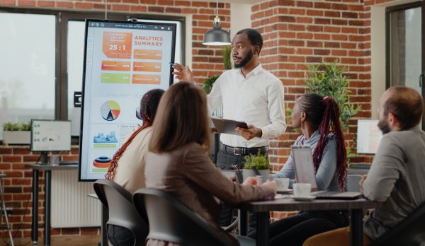 Company employee presenting business strategy with charts on monitor, planning project. Workmates analyzing financial statistics on display, working together on company development.