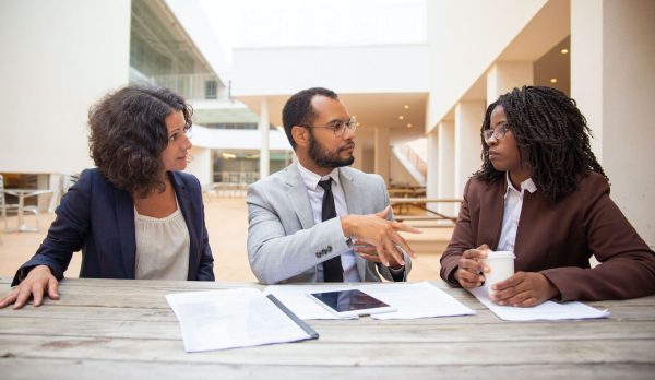 Business colleagues discussing project reports in street cafe. Business man and woman sitting at table with papers and tablet and talking. Paperwork or teamwork concept