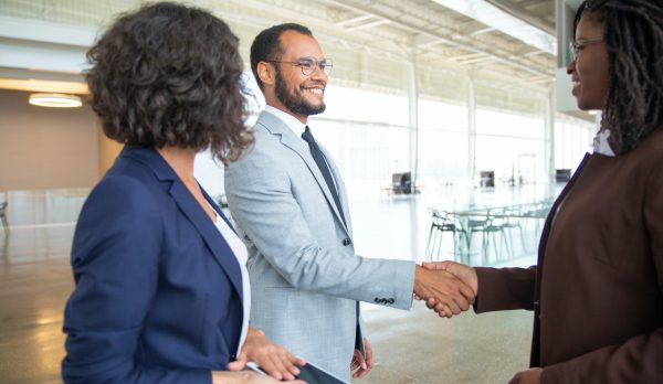 Cheerful business people shaking hands. Businesswoman holding digital tablet and looking at smiling business colleagues shaking hands in office. Cooperation concept