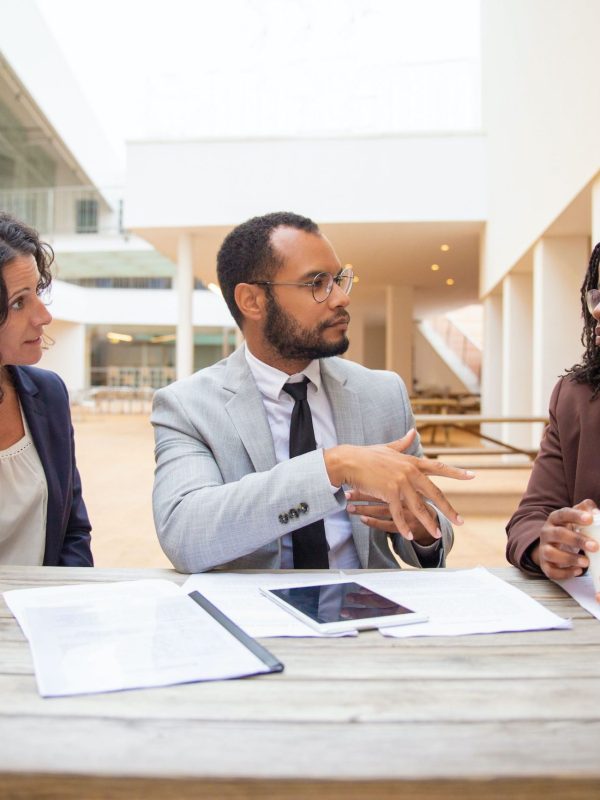 Business colleagues discussing project reports in street cafe. Business man and woman sitting at table with papers and tablet and talking. Paperwork or teamwork concept