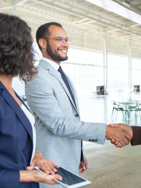 Cheerful business people shaking hands. Businesswoman holding digital tablet and looking at smiling business colleagues shaking hands in office. Cooperation concept