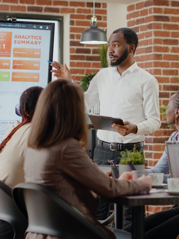 Company employee presenting business strategy with charts on monitor, planning project. Workmates analyzing financial statistics on display, working together on company development.